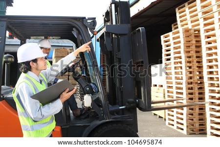 workers at unloading works with forklift loader in warehouse