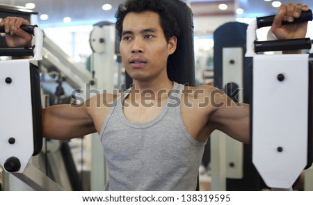 asian man exercising on machines at modern gym - health club