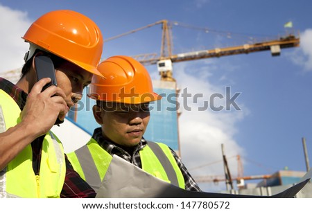 Construction worker looking at blueprint at construction site and one people talking on the phone