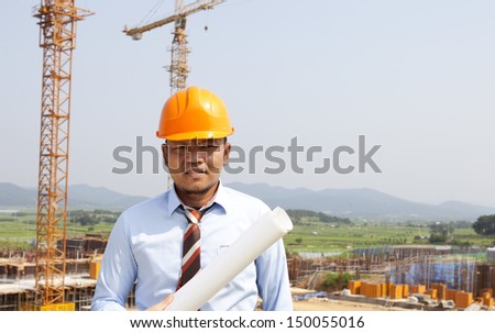 Asian man architect on location site and yellow cranes on the background