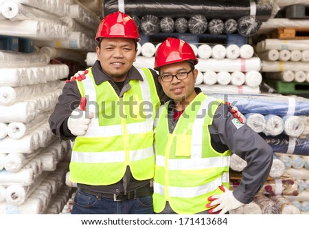Two textile factory workers standing in  warehouse raw material fabrics with giving thumb up