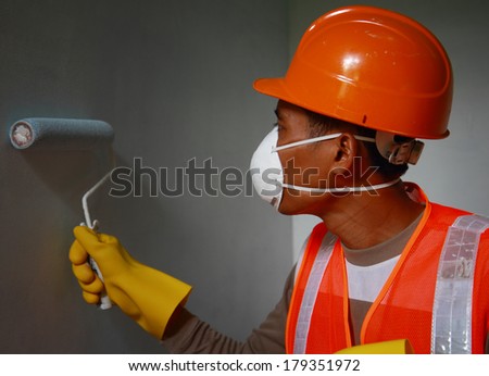 Painter worker wearing safety mask or safety work on job, painting of building house or apartment wall with roll