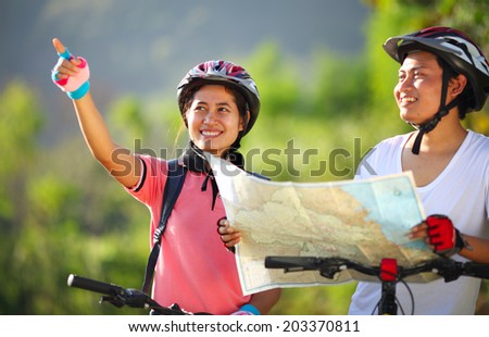 Happy young couple riding a bike with map looking and pointing