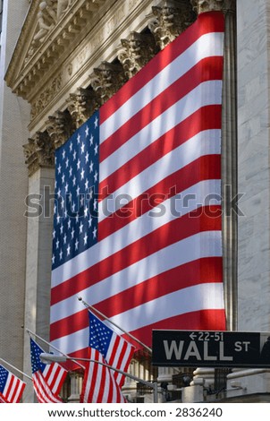 Lovely sun-dappled view of the historic New York Stock Exchange building draped in an American flag, with Wall Street street sign, full field focus.