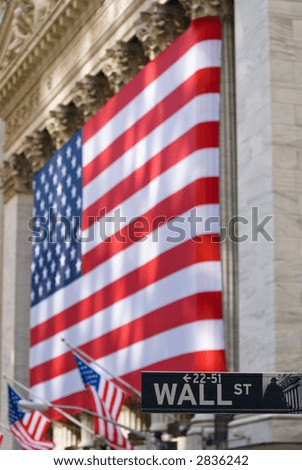 Wall Street street sign with lovely sun-dappled view of the historic New York Stock Exchange building draped in an American flag, foreground focus.