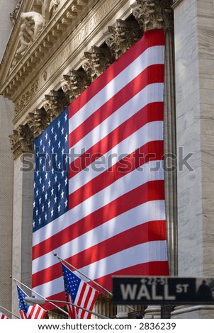 Wall Street street sign with lovely sun-dappled view of the historic New York Stock Exchange building draped in an American flag, background focus.