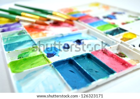 Colorful watercolor palette and different type of paintbrushes on white background