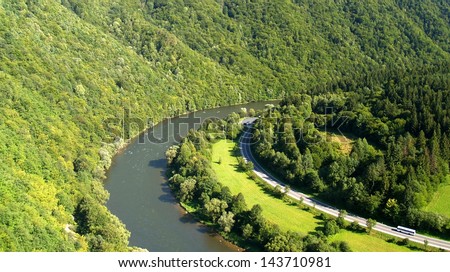 Scenic aerial view of road by river in countryside with forested mountain; Slovakia.