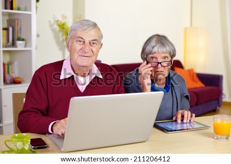 Happy elderly couple having fun with technology tablet and pc