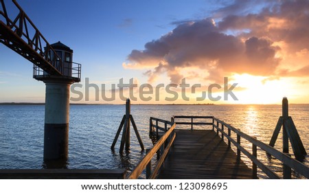 Jetty and light beacon at the shore during a cold and colorful sunrise.