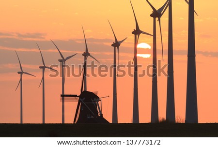 Modern wind turbines and a traditional windmill in the Netherlands at a beautiful sunset.