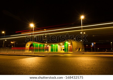 Bus driving by a colorful bus stop at night. Long exposure.