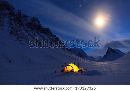 Tent in the snow covered mountains of Lapland on a beautiful winter night with moon and stars.