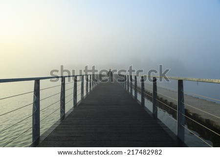 Man walking on a footbridge into the morning fog.