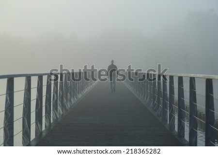 Man walking on a footbridge into the morning fog.