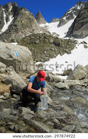 Hiker woman taking water from river in the Swiss mountains on an hiking adventure.