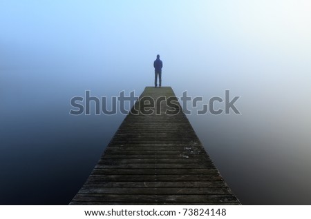 Man standing alone on the end of a jetty, looking into the fog.