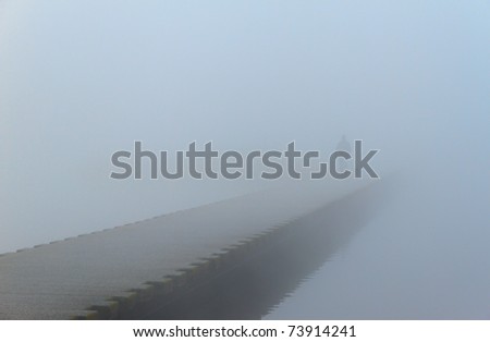 Man walking with his dog on a jetty, in the dense fog.