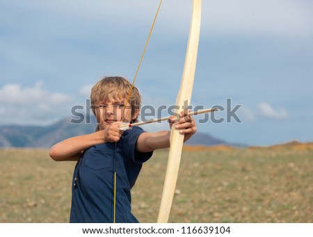 Boy shoots a bow at a target, in the open air
