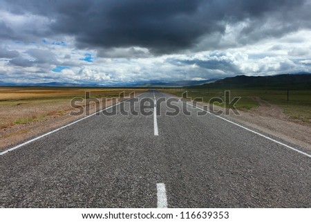 An empty desert road with dark and foreboding storm clouds on the horizon.