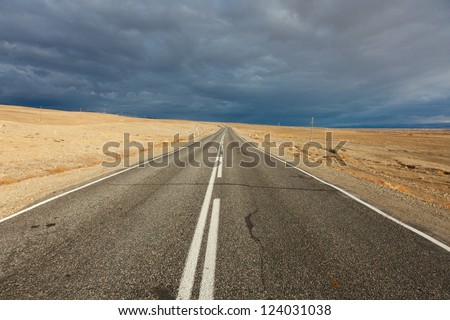 An empty desert road with dark and foreboding storm clouds on the horizon.