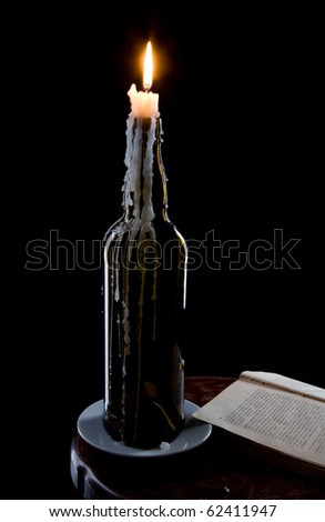 A candle in a bottle and a book on black