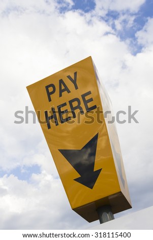 Yellow \'Pay Here\' sign above the car park ticket machine in a UK car park.