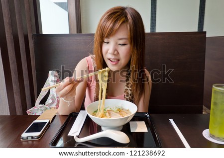 A cute Thai girl is eating a Japanese Ramen in the resturant. This is urban life.