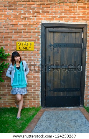 Cute Asian Thai woman is standing outside the room with staff only label sign on the wall with old retro design interior. Is she a staff or an employee of this office restricted area?