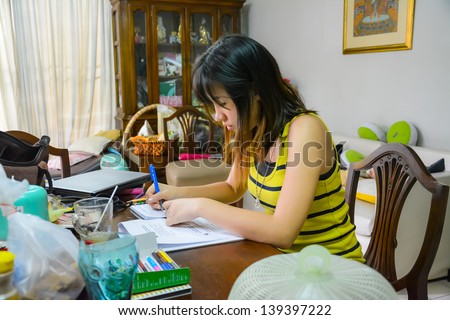Thai college girl is busy studying in a messy desk with concentration.