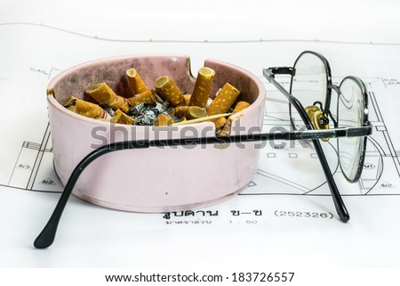 Ashtray and glasses on white blueprint background (in Thai language) representing stress in work concept.