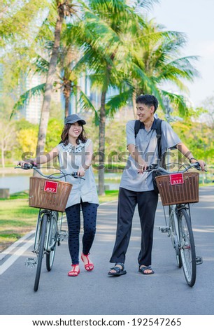 A friend couple are walking and chatting with bicycle in the park