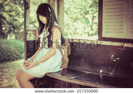 Cute Asian Thai girl in vintage clothes is waiting alone in an old bus stop in bright vintage color tone