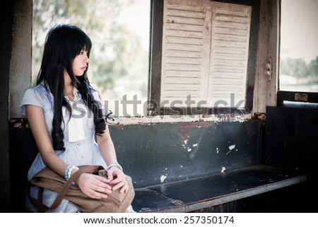 Cute Asian Thai girl in vintage clothes is waiting alone in an old bus stop in retro color tone