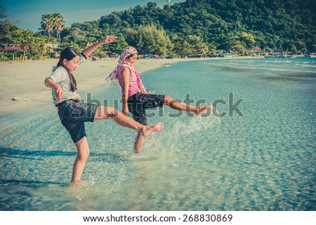 Two Asian Thai girls are kicking the sea along the beach coast of Rayong, Thailand in childhood color