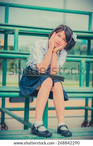 Shy Thai schoolgirl sitting on a metal stand in childhood theme