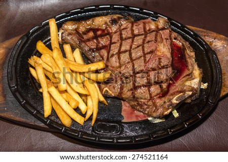 Premium American prime rib steak with french fries on a metal plate ready to serve. The focus is shallow depth of field.