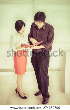 Thai (Asian) boss is ordering a task for his cute secretary in the office in vintage color. It is teamwork concept.