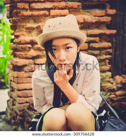 Cute Asian Thai girl is sitting and making a surprise expecting facial expression in vintage color style. Focus on model face.