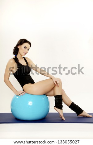 Attractive young brunette sporty woman in black dress with blue fitness ball isolated on white background