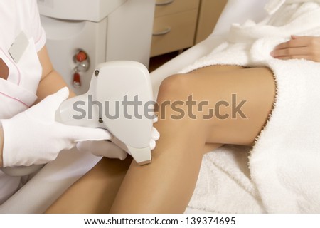 Young brunette woman receiving laser therapy removal on legs. Spa studio shot