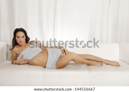 Beautiful and attractive sexy sensuality female young adult brunette woman posing in blue blanket on the white sofa