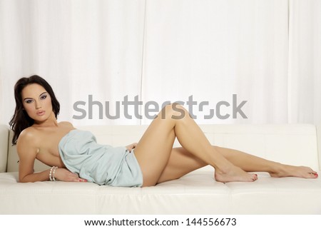 Beautiful and attractive sexy sensuality female young adult brunette woman posing in blue blanket on the white sofa