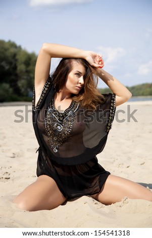 Young adult attractive beautiful brunette woman in black transparent blouse on the beach