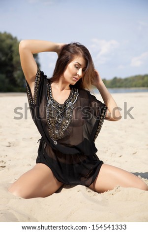 Young adult attractive beautiful brunette woman in black transparent blouse on the beach