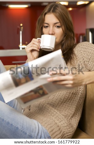 young adult beautiful brunette woman drinking coffee and reading newspaper in luxury apartment
