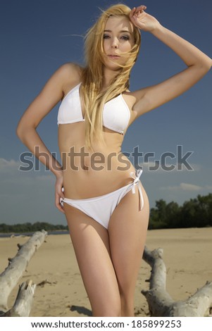 beautiful blonde woman in white bikini posing on a log