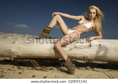 beautiful young adult attractive and sensuality pretty blonde woman in white bikini posing on a log on the beach
