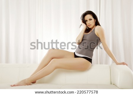 Beautiful sensuality and attractive sexy female young adult brunette woman posing in grey shirt on the white sofa
