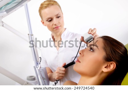 Young adult brunette pretty woman getting laser face treatment in medical spa center, skin rejuvenation concept